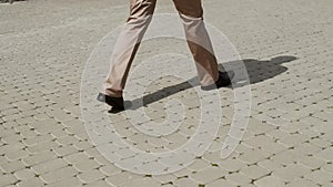 Man legs of guy in black shoes and brown trousers walk on gray paving slabs