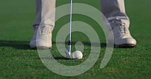 Man legs swinging golf putter club on course field. Player feet stand on grass.