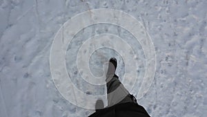 Man legs walking through the snow at winter wearing black boots and green pants. Hiking shoes POV walk on snow on winter