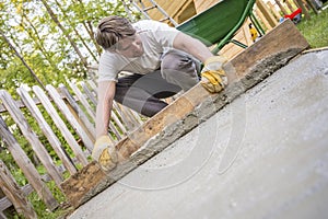 Man leveling the cement in a backyard at home using a wooden plank