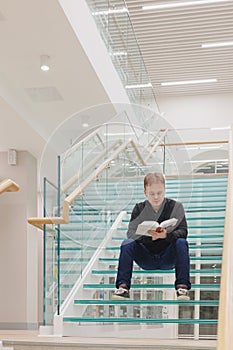 man in library is reading book sitting on steps of glass staircase