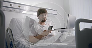 Muž spočívá na postel a chatování telefon v nemocnice 