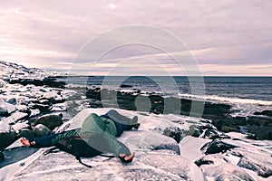 man lies on the seashore in winter in the snow. Vacation by the Arctic Ocean. A tired traveler is resting.
