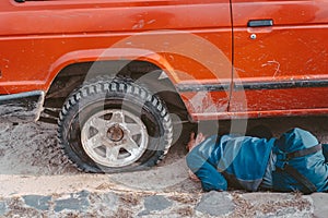 Man lies under a 4x4 car on a dirt road