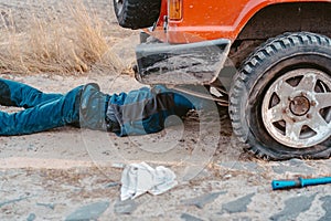 Man lies under a 4x4 car on a dirt road