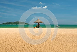 A man lifeguard, sitting under an umbrella of palm leaves on a deserted beach of Hainan Island.