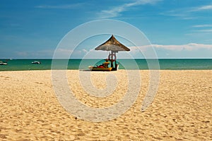 A man lifeguard, sitting under an umbrella of palm leaves on a deserted beach of Hainan Island.