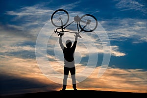 Man lifting bicycle at sunset sky.