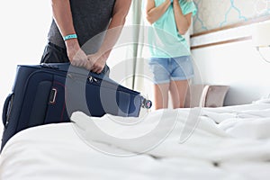 Man lifting heavy suitcase in front of woman in hotel room closeup