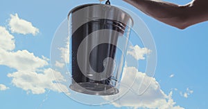 Man lifts Leaking bucket with water dripping, blue sky clouds, Lost opportunity.