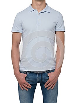 A man in a light blue polo shirt and denims holds his hands in pockets.
