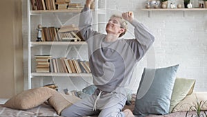 a man in light pajama clothes is sitting in bed in the morning, closing his laptop and happily jumping and enjoying life