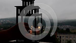 Man is lighting candle in lantern on the terrace. Cloudy background.