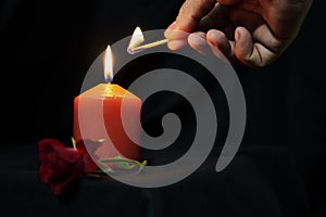 a man lights a red candle with a match and a red rose on a black background copy space gothic style