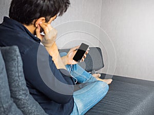 Man listen to music from phone using earphone on sofa