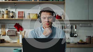Man listening educational seminar in kitchen with headphones. Student studying.