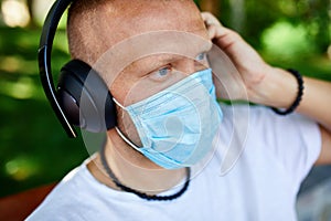 Man listening music with headphone, wearing protective mask outdoor photo