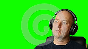 Man is listening music with headphones at green screen background.