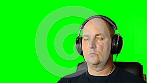 Man is listening music with headphones at green screen background.