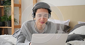 Man listening music on headphones while using laptop on bed