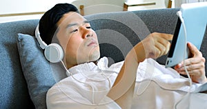 Man listening to music on digital tablet while lying on sofa 4k