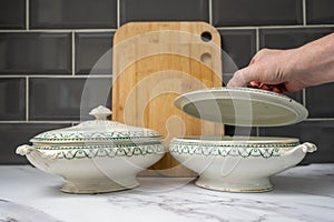 man liting the lid on a tureen in the kitchen on a marble worktop