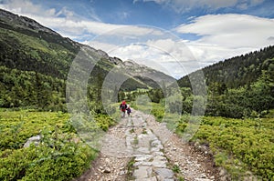 Man and little girl go on the mountain trail between two mountain range