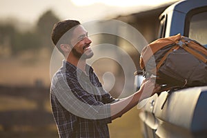 Man Loading Backpack Into Pick Up Truck For Road Trip To Cabin In Countryside