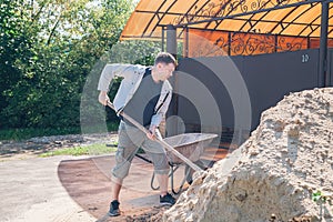 A man loads sand onto a garden wheelbarrow to fill the paths with concrete