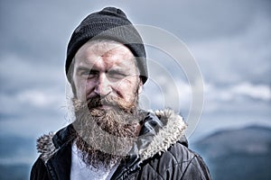 Man with long beard and mustache wears hat. Hipster on strict face with beard looks brutally while hiking. Masculinity