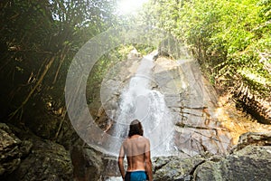 Man with a long hair is enjoy in lagoon of huge tropical waterfall in jungle. Travel concept.