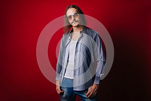 A man with long hair in a plaid shirt and white T-shirt, in blue jeans. The guy with the mustache and dark glasses is dressed in