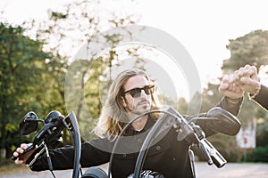 Man with long hair waving to another person in a motorcycle