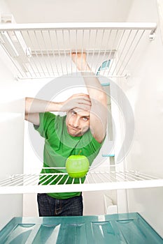 Man looking at apple in fridge