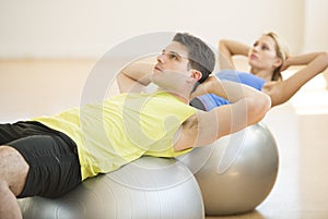 Man Looking Away While Exercising On Fitness Ball At Gym
