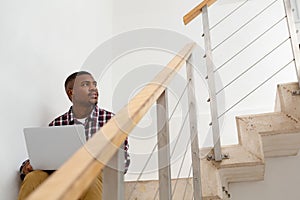 Man looking away while working on laptop on stairs in a comfortable home