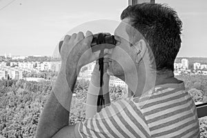 A man looking through the binoculars from the balcony.