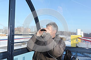 The man looking in binoculars from a ferris wheel cabin