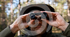 man looking through binoculars in forest. park monitoring, birdwaching
