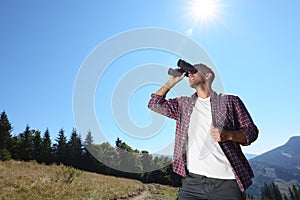 Man looking through binoculars in mountains on sunny day, low angle view