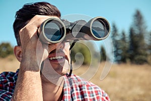 Man looking through binoculars outdoors on sunny day