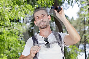 man looking through binoculars in woods