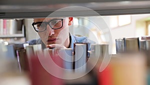 Man Looking For Book On Bookshelves At Library At College