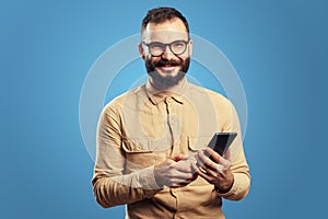 Man looking at camera while holding mobile phone,  over blue background