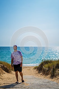 man looking at camera strolling along wooden path on the beach