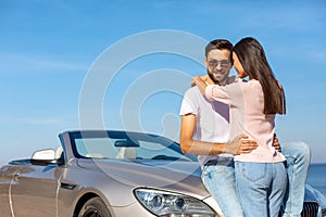 Man looking at the camera while woman embracing him and leaning convertible