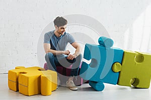 Man looking at connected blue and green jigsaw pieces while sitting near brick wall