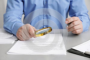 Man looking at document through magnifier at white table, closeup. Searching concept