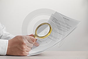 Man looking at document through magnifier at white wooden table, closeup. Searching concept