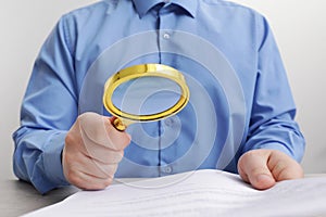 Man looking at document through magnifier at white wooden table, closeup. Searching concept